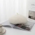 Weiche cremefarbene Wollbaskenmütze auf einer offenen Zeitschrift in Lifestyle-Umgebung - Weiß