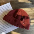 Detail van een verweerde bordeauxrode gebreide muts met zilveren ringen en speld. - Bordeauxrood
