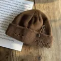 Detailopname van bruine gebreide muts met veiligheidsspeld en ringen op houten ondergrond - koffiekleur