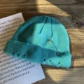 Detail van turquoise gebreide muts met zilveren ringen, veiligheidsspeld en gaten. - Meerblauw