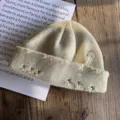 Gedetailleerd aanzicht van gebreide muts met veiligheidsspeld en zilveren ringen - Beige
