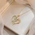 Dettaglio macro della collana con ciondolo a cuore dorato, pietre verdi e incisione LOVE - X1054 / Smeraldo