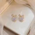 Élégantes boucles d'oreilles nœud dorées avec zircons brillants dans une boîte à bijoux - Nœud Papillon Or (E0039)