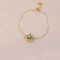Gros plan d'un bracelet doré ajustable avec un charmant pendentif fleur verte rotatif - Vert