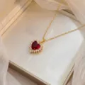 Primer plano detallado de un collar de corazón dorado con piedra roja en un joyero - Estilo Corazón Geométrico Rubí (X2446)