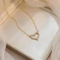 Primer plano de collar con colgante de corazón dorado brillante con circonitas en caja - Estilo Pavé Strass Blanco Clásico (X0930)