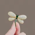 Exquisite gold-tone dragonfly brooch featuring sparkling green and white crystals. - Dragonfly