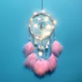 Nahaufnahme eines rosa Traumfängers mit leuchtenden LED-Lichtern und weichen Federn. - Hängelampe in Mondlicht-Rosa