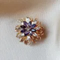 Elegant flower-shaped brooch pin featuring purple and clear marquise crystals in gold setting - White And Purple