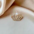 Macro detail of a sparkling golden crown brooch with rhinestones and a white pearl bead. - Luxury Crown Style (838) / Crown