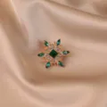 Detailed macro view of vintage flower brooch with green crystals on champagne silk fabric - Green Floral
