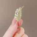 Detail view of an elegant gold leaf-shaped brooch adorned with sparkling crystals - Gold Metal Base Leaf Shaped / Leaf