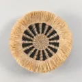 Dettaglio della decorazione murale rotonda in paglia boho con motivo nero e frange in rafia. - C1