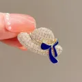 Detail view of a sparkling crystal hat-shaped brooch with an elegant blue bow decoration - Gold Hat