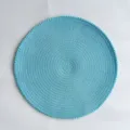 Vista dettagliata di una tovaglietta rotonda azzurra intrecciata con bordo di pompon. - 38 cm / Blu
