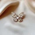 Close-up detail of the elegant butterfly brooch, shimmering rhinestones with central pearl. - Gold