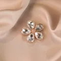 Crystal flower brooch detail shot showcasing the sparkling pear-shaped rhinestones and golden metallic setting. - White
