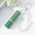 Macro detail of luxury green rhinestone perfume atomizer with white pearl keychain. - Green