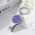 Detail of silver nail clipper keychain with purple rhinestones on white stone - Purple