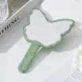 Dettaglio ravvicinato degli strass verdi su uno specchio da trucco a mano a forma di farfalla - Verde