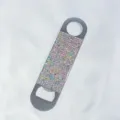 Detailed view of a portable rhinestone-encrusted beer bottle opener on white silk. - AB White