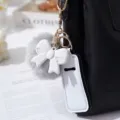 Close-up of white bow and grey pom-pom keychain set hanging on a black bag. - White