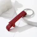 Close-up detail of a red rhinestone-encrusted bottle opener keychain with a silver ring - Red