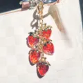 Detail showing a bunch of red resin strawberry charms hanging on a white bag - Transparent Red