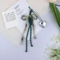 Detail view of a woven bow keychain with a shiny silver heart charm on white fabric - Green Bow Silver Heart (2) / Dark Green