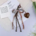 Detailed view of a brown cotton rope bow keychain with a resin heart pendant charm. - Coffee