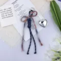 Detail view of a woven cotton rope bow bag charm with a silver heart pendant. - Dark Blue Purple