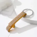 Detailed close-up of a rhinestone-studded gold-toned aluminum beer bottle opener keychain. - Gold