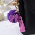 Close-up of purple pompom and bow keychain with lipstick holder on a black bag - Deep purple