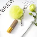 Detalle de frasco de perfume con pedrería, pompón de piel amarilla y llavero con silbato - Juego de Colgantes de 3 Piezas / Dorado