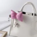 Detail of a puffy pink bow keychain with a silver heart charm on a white handbag - Pink