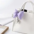 Close-up detail of purple puffed leather bow keychain with silver heart charm on white bag - Purple