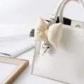 Detail of cream leather bow keychain with silver heart charm on a bag - Off White