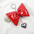 Close-up of shiny red leather puffed bow keychain with silver heart charm and tag. - Angola Red