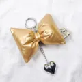 Macro view of a stylish metallic gold padded bow keychain featuring a silver heart charm. - Gold