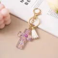 Close-up of transparent resin cross keychain with embedded purple flowers and tassel. - Purple Dried Flower (White Tassel)