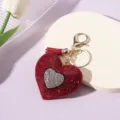 Close-up of sparkling rhinestone heart keychain with a vibrant red tassel detail. - Red