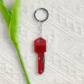 Red key-shaped mini folding knife keychain shown in detail on white patterned fabric - Red