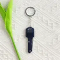 Close-up of a black key-shaped folding pocket knife on a textured background - Black