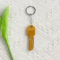 High-quality detailed view of a golden key-shaped mini pocket knife keychain on white fabric - Gold