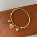 Detailansicht eines 18K vergoldeten Armreifs aus Edelstahl mit drei Herzanhängern und Kristallen - Einfacher Herz-Anhänger-Stil / Gold