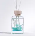 Botella difusora de vidrio con elementos botánicos azules y varillas difusoras. - Jacinto Silvestre