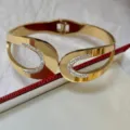 Modisches breites goldfarbenes Titanstahlarmband besetzt mit weißen Strasssteinen. - Doppel-C Hohlstil / Gold