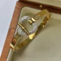 Elegantes goldfarbenes Herzarmreif aus Edelstahl mit Pavé-Kristallen in einer Schmuckschatulle - T-Bar Herz Strass Stil
