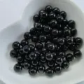 Gros plan detaille de perles rondes noires et lisses dans un plat blanc pour vos bijoux DIY. - Sans Trou / Agate noire