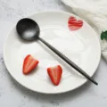 Schwarzer Löffel aus Edelstahl mit weißem Keramikteller und rotem Herzmuster für elegante Tische. - Speiselöffel / Schwarz